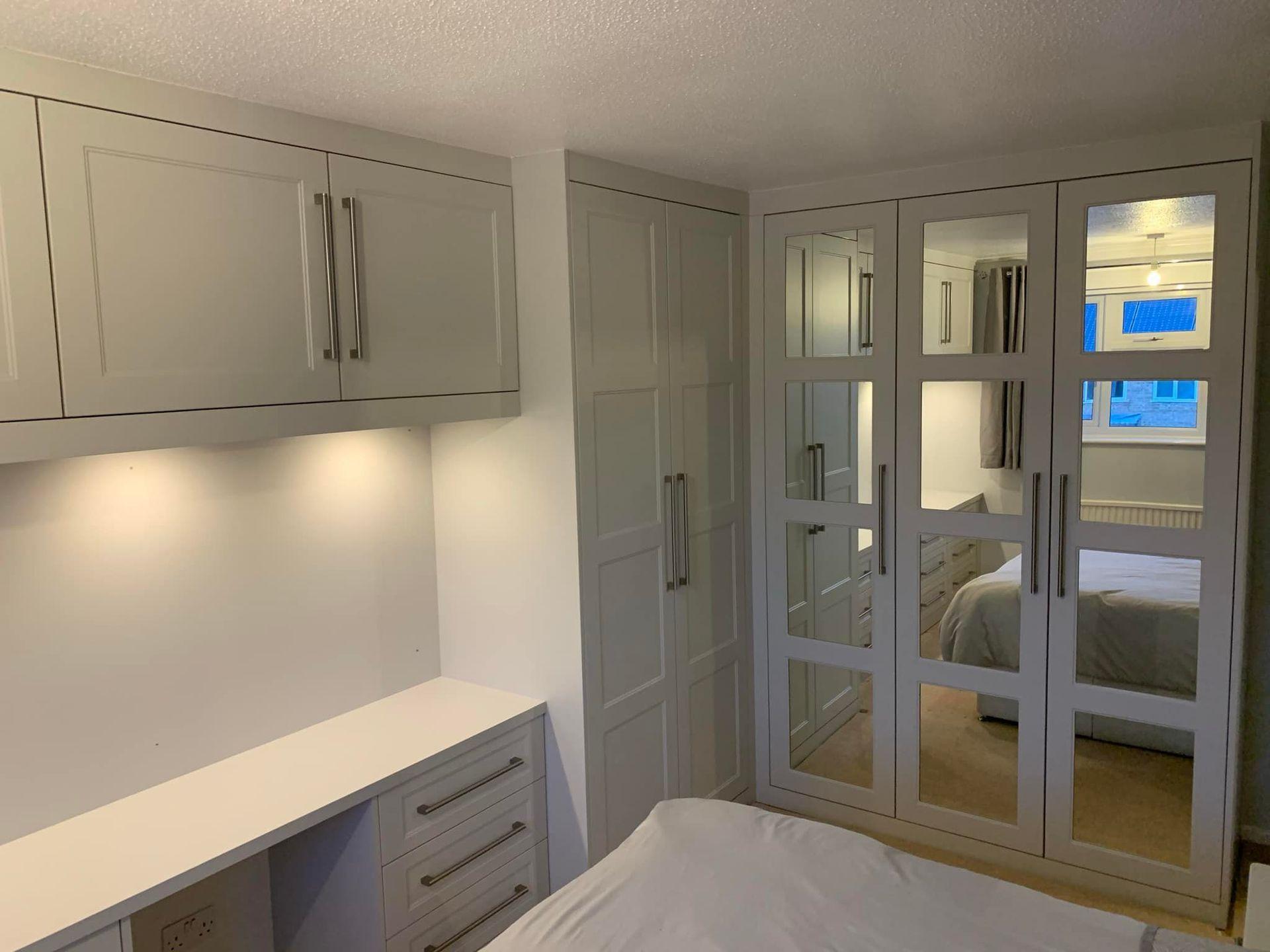 Modern bedroom with mirrored wardrobe doors, white cabinets, and ambient lighting.