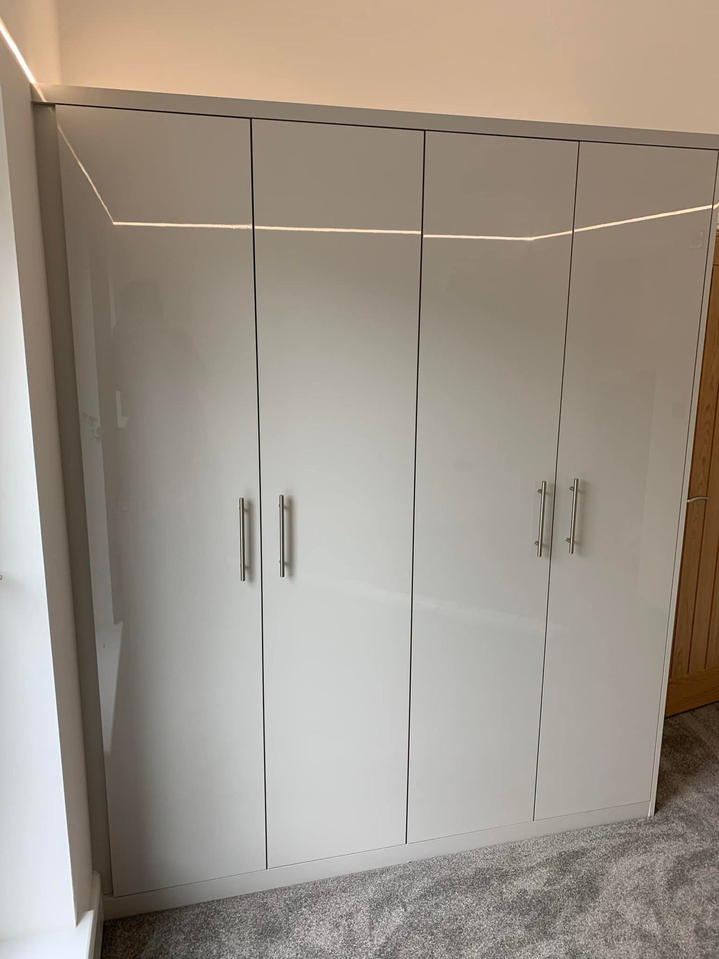 Modern white glossy wardrobe with sleek silver handles, situated in a carpeted room with soft lighting.