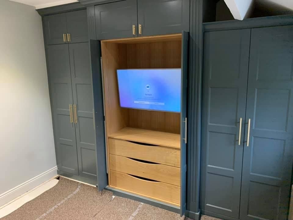 Built-in wardrobe with open section revealing a TV and drawers.