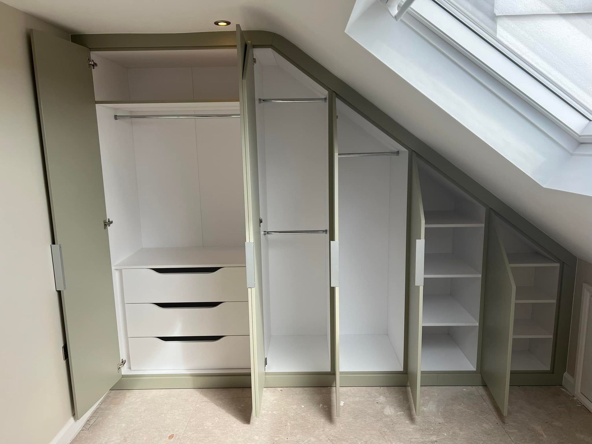 Custom built-in wardrobe under sloped ceiling with open doors revealing storage spaces and drawers.